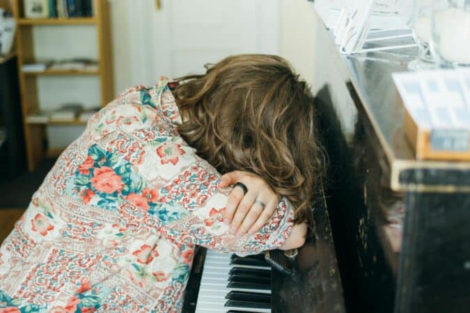 A woman leans asleep on a piano, illustrating fatigue or relaxation in a cozy indoor setting.